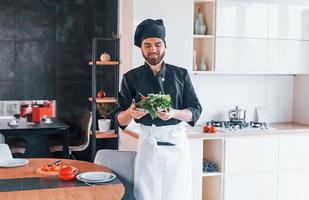 cozinheiro profissional jovem chef de uniforme fazendo salada na cozinha foto