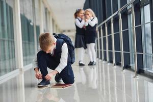 menino sentado no chão. crianças da escola de uniforme juntos no corredor foto