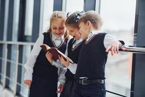 crianças da escola de uniforme lendo livro juntos no corredor. concepção de educação foto