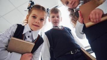 crianças da escola de uniforme posando para uma câmera juntos no corredor. concepção de educação foto