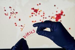 a mão do homem segura a lente com o título do vírus contra o fundo com o mapa-múndi da infecção foto