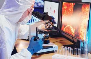 cientista em uniforme protetor branco perto de monitores com dados trabalha com coronavírus e tubos de sangue em laboratório foto