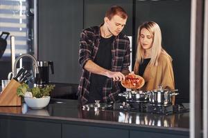 jovem casal em roupas casuais juntos na cozinha e preparando comida foto