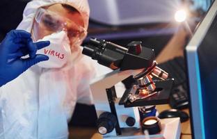 cientista em roupa de proteção branca dentro de casa em laboratório com lente com título de vírus nele foto