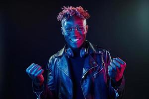 óculos elegantes e fones de ouvido sem fio. iluminação neon futurista. jovem afro-americano no estúdio foto