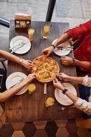visão aproximada de pessoas que pegam e comem pizza dentro de casa juntos foto