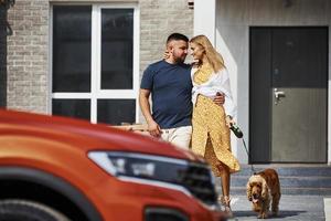 lindo casal tem um passeio junto com cachorro ao ar livre perto do carro foto