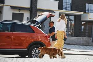 porta-malas está aberto. lindo casal tem um passeio junto com cachorro ao ar livre perto do carro foto