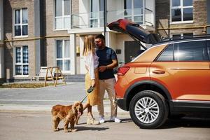 porta-malas está aberto. lindo casal tem um passeio junto com cachorro ao ar livre perto do carro foto