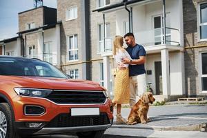 abraçando um ao outro. lindo casal tem um passeio junto com cachorro ao ar livre perto do carro foto