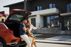 porta-malas está aberto. lindo casal tem um passeio junto com cachorro ao ar livre perto do carro foto