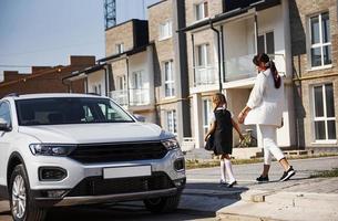 mãe com filha em uniforme escolar ao ar livre perto de carro branco foto