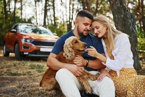 casal com cachorro tem fim de semana ao ar livre na floresta com carro atrás deles foto