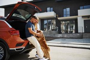 porta-malas está aberto. lindo casal tem um passeio junto com cachorro ao ar livre perto do carro foto