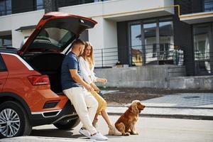 porta-malas está aberto. lindo casal tem um passeio junto com cachorro ao ar livre perto do carro foto