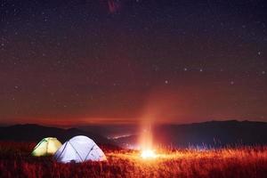 duas tendas iluminadas com fogueira sob as estrelas nas montanhas à noite foto