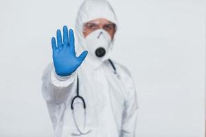mostra o gesto de parada à mão. cientista médico masculino em jaleco, óculos de proteção e máscara foto