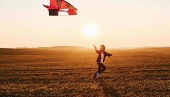 menina feliz correndo com pipa nas mãos no belo campo na hora do nascer do sol foto