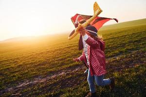 menina bonitinha corre com avião de brinquedo no belo campo durante o dia ensolarado foto