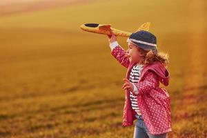 menina bonitinha divirta-se com o avião de brinquedo no belo campo durante o dia ensolarado foto