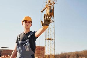 mostra o sinal de parada à mão. trabalhador da construção civil em equipamentos uniformes e de segurança tem trabalho na construção foto