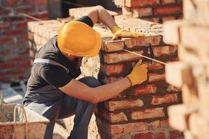 medidas de parede de tijolo. trabalhador da construção civil em equipamentos uniformes e de segurança tem trabalho na construção foto