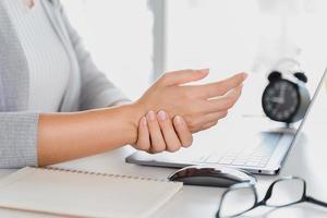 mulher closeup segurando sua mão dor de usar o computador portátil muito tempo. conceito de síndrome de escritório. foto