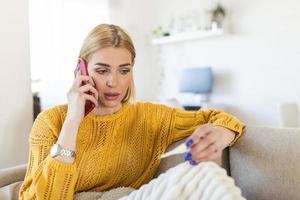 jovem está olhando para o termômetro. ela está com febre, ligando para o médico. mulher bonita com sintomas ligou para o número de emergência covid-19 para relatar suas condições médicas foto