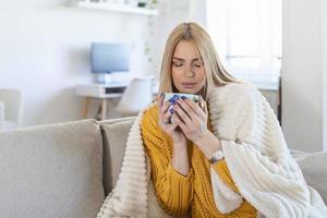 linda mulher elegante sentada em casa pensando, humor melancólico romântico, vestindo suéter de malha, sentindo-se quente, estilo de inverno, bebendo café, coberto com cobertor de lã foto