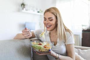 mulher de estilo de vida saudável comendo salada sorrindo feliz ao ar livre em um lindo dia. jovem fêmea comendo comida saudável rindo e relaxando no sofá.