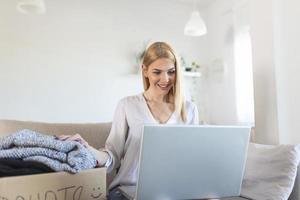 conceito de doação. mulher segurando uma caixa de doação cheia de roupas. mulher segurando um livro e roupas doam caixa. roupas em caixa para doação de conceito e reciclagem de reutilização foto