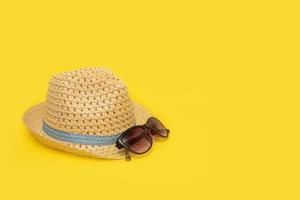 chapéu de palha e óculos de sol em um fundo amarelo com espaço de cópia foto
