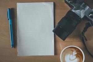 vista superior do papel vazio, xícara de café, câmera e caneta na mesa de madeira foto