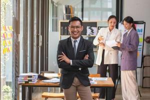 marketing, financeiro, contabilidade, planejamento, empresário sorridente em pé com os braços cruzados alegremente liderando uma equipe de gerenciamento de negócios lucrativos dentro do escritório. foto