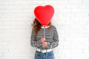jovem mulher engraçada escondida atrás do balão de coração conceito de dia dos namorados foto