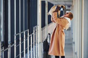 jovem passageira em roupas quentes andando com seu cachorro no saguão do aeroporto foto