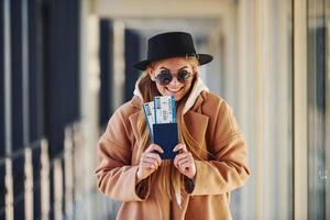 jovem passageira em roupas quentes, mostrando bilhetes no saguão do aeroporto foto