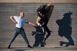 lindo casal em roupas pretas dançando juntos contra a parede ao ar livre foto