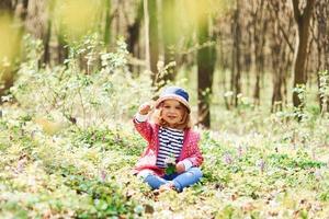 menina feliz de chapéu azul tem caminhada na floresta de primavera durante o dia foto