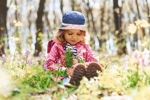 menina feliz de chapéu azul tem caminhada na floresta de primavera durante o dia foto