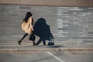 em máscara protetora. bela morena com cabelos cacheados e roupas pretas correndo ao ar livre perto da parede foto