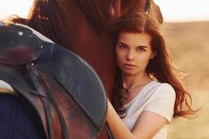 jovem mulher abraçando seu cavalo no campo agrícola durante o dia ensolarado foto