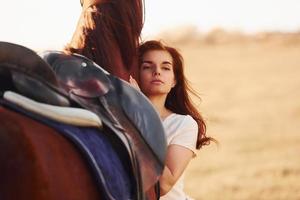 jovem mulher abraçando seu cavalo no campo agrícola durante o dia ensolarado foto