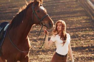 jovem de pé com seu cavalo no campo agrícola durante o dia ensolarado foto