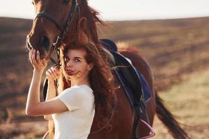 jovem mulher abraçando seu cavalo no campo agrícola durante o dia ensolarado foto
