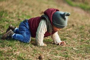 menino em roupas quentes, deitado no chão do campo na grama foto