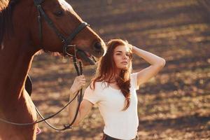 jovem de pé com seu cavalo no campo agrícola durante o dia ensolarado foto