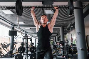 barra de levantamento. jovem esportivo forte em roupas pretas tem dia de treino na academia foto