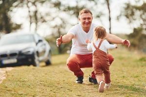 pai em roupas casuais caminha e se diverte com a filha ao ar livre perto da floresta foto