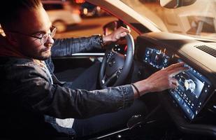 usando a tela de navegação. homem bonito de barba por fazer em roupas da moda andando de automóvel foto